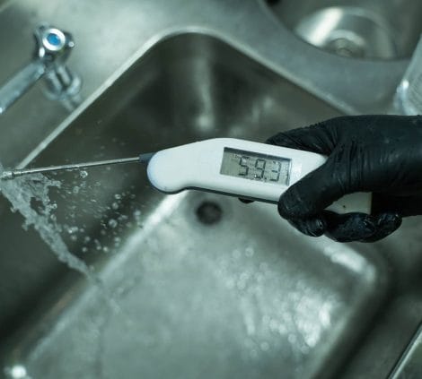 Gloved technician taking hot water temperature reading of 59.3°C at a running sink tap during Legionella monitoring