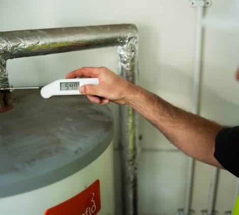 Water hygiene engineer measuring calorifier flow temperature at 54.8°C using a digital thermometer on lagged pipework