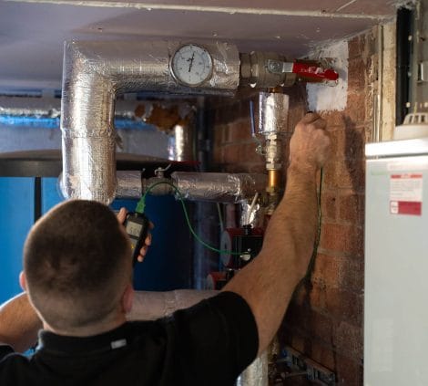 Water hygiene engineer taking temperature readings from insulated hot water pipework in a commercial plant room