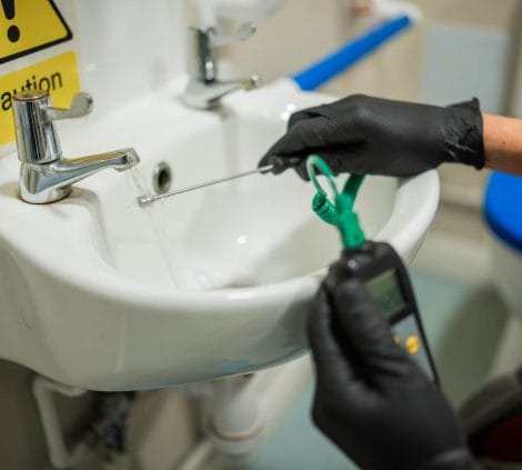 Engineer measuring water temperature at a tap for Legionella control checks
